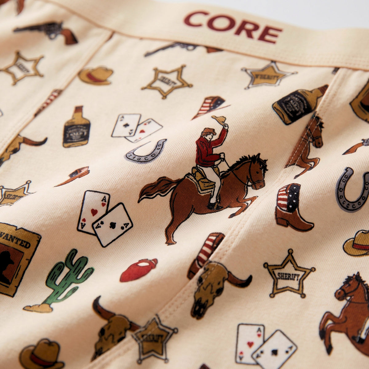 Close-up of CORE Western print fabric with cowboy, horseshoe and boot artwork